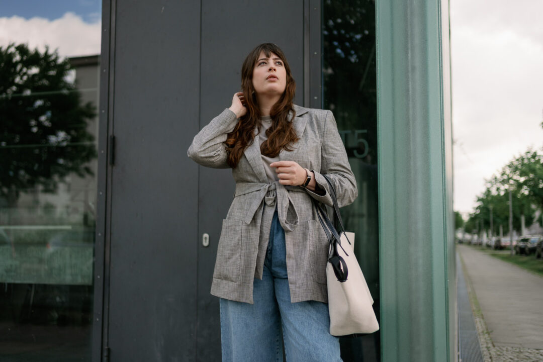 Andrea trägt eine weite Jeans mit grauem Oversize-Blazer, weißen Sneakern und cremefarbener Tote Bag – perfekter Casual-Business-Style für den Alltag.
