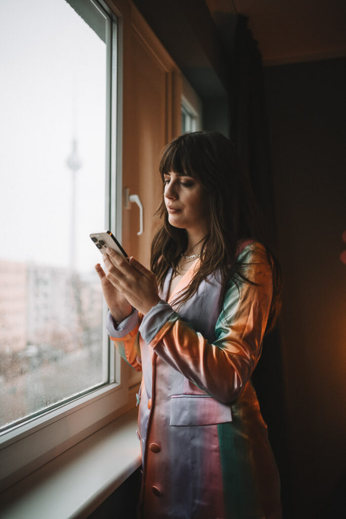 am Fenster mit dem Handy nach Anschluss in Berlin suchend