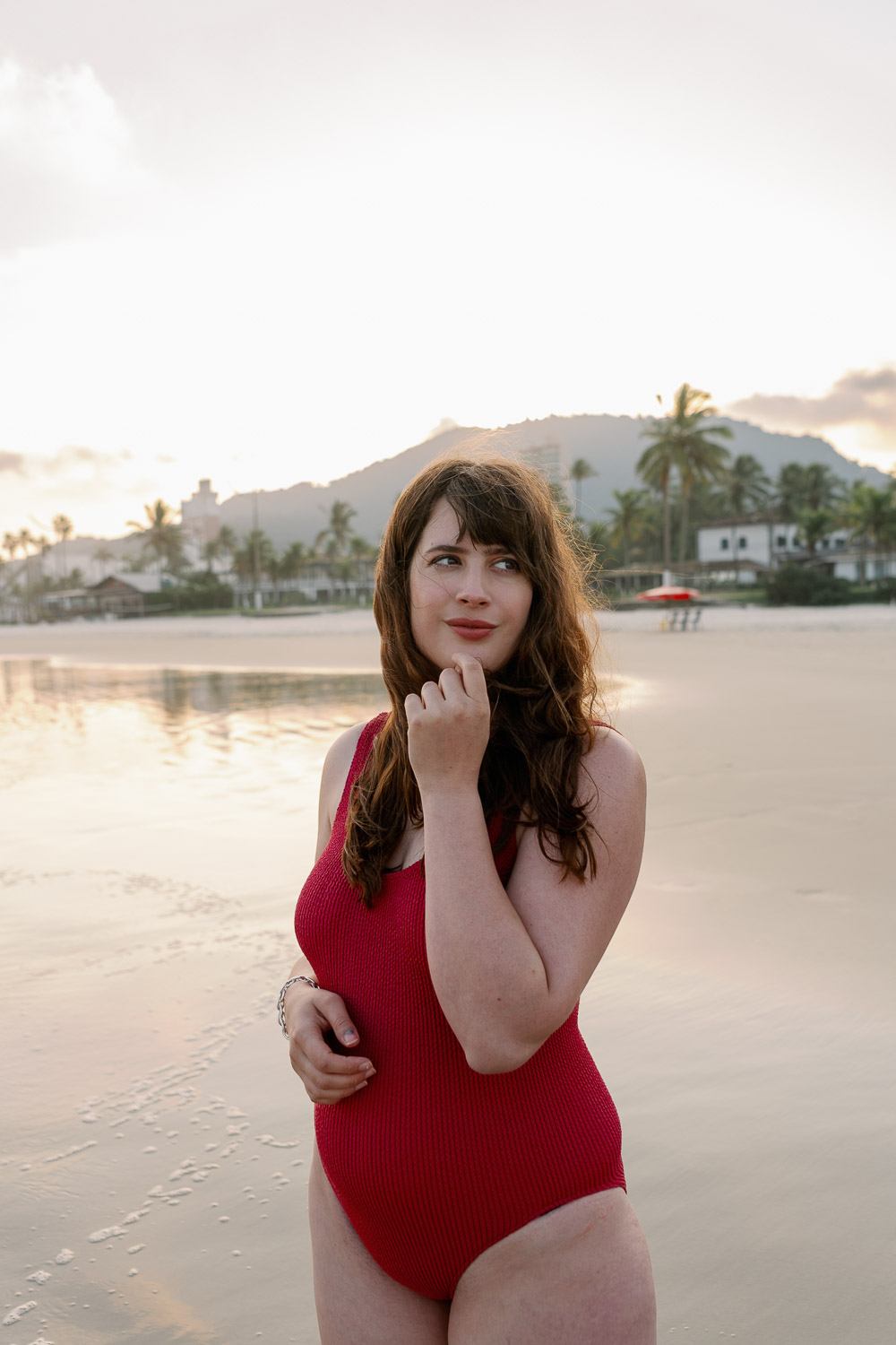 Andrea von andysparkles im roten Badeanzug am Strand bei Sonnenuntergang, lächelnd und mit der Hand am Kinn – bequemer Badeanzug nach der Schwangerschaft