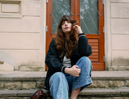Streetstyle Herbst 2025: Andrea im Collegelook mit schwarzer Jacke, Culotte-Jeans und Loafers, die bordeauxrote Tasche bringt Farbe ins Outfit.