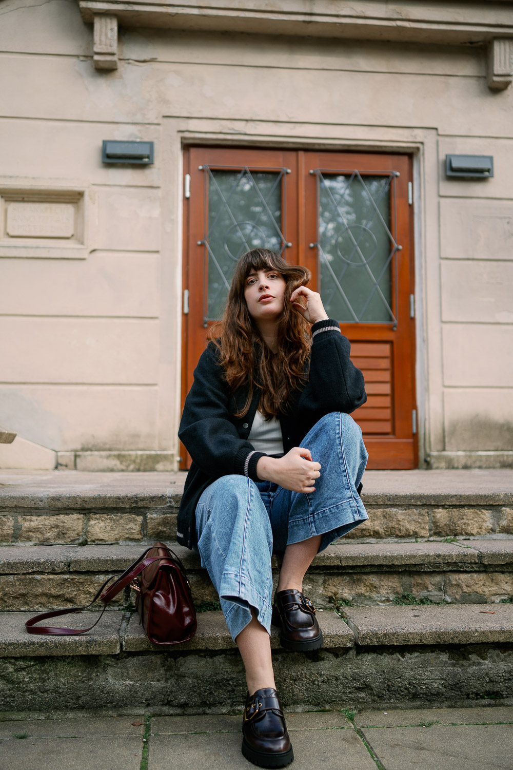 Streetstyle Herbst 2025: Andrea im Collegelook mit schwarzer Jacke, Culotte-Jeans und Loafers, die bordeauxrote Tasche bringt Farbe ins Outfit.