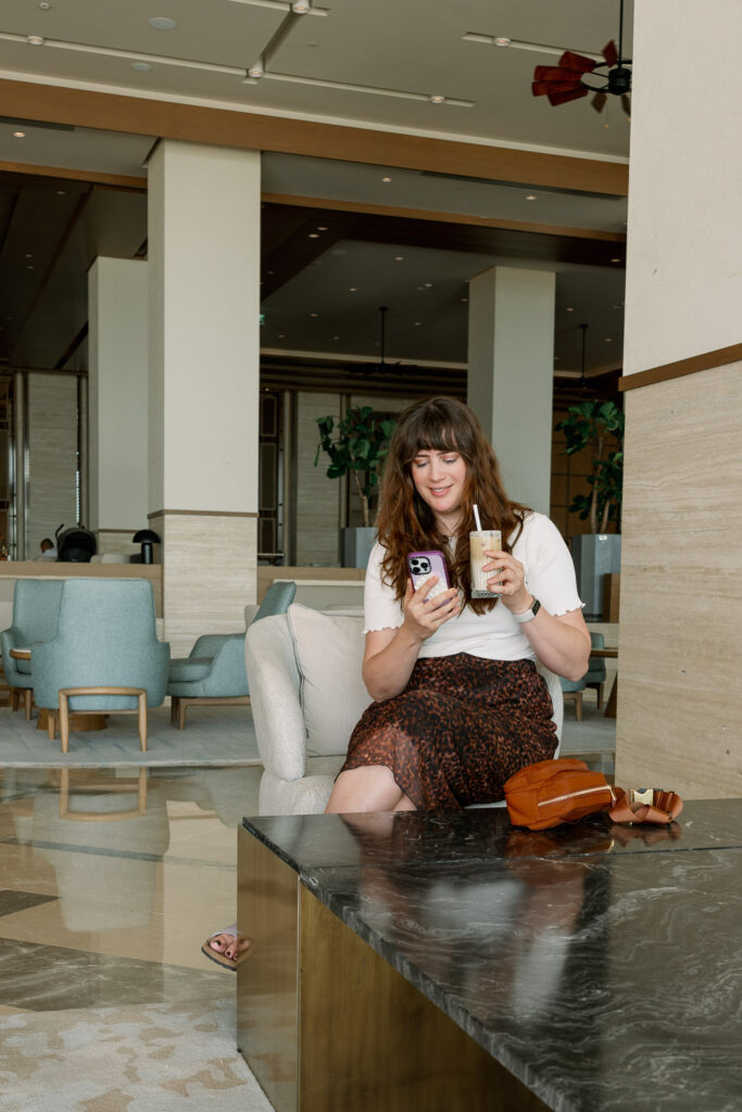 Andrea von andysparkles sitzt mit Smartphone und Eiskaffee in moderner Hotel-Lounge – Blogartikel über Cybersecurity und Hackerschutz