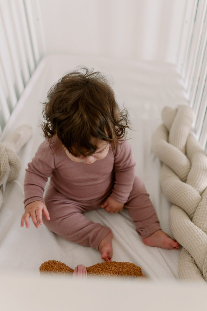 Baby Dottie sitzt im Kinderbett und spielt – neugierig auf die ersten Beikost-Erfahrungen.
