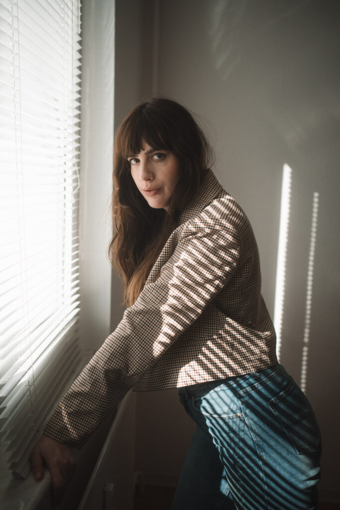 Andrea Funk von andysparkles lehnt am Fenster, Jeans und karierter Blazer – Ruhe, Natürlichkeit und meine vereinfachte Hautpflegeroutine