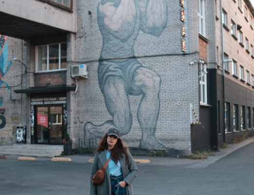 Streetstyle mit Jeans im Winter: Andrea spaziert durch das Telliskivi-Viertel in Tallinn, trägt eine Paperbag-Jeans, grauen Mantel und Sneaker vor urbaner Streetart-Kulisse.