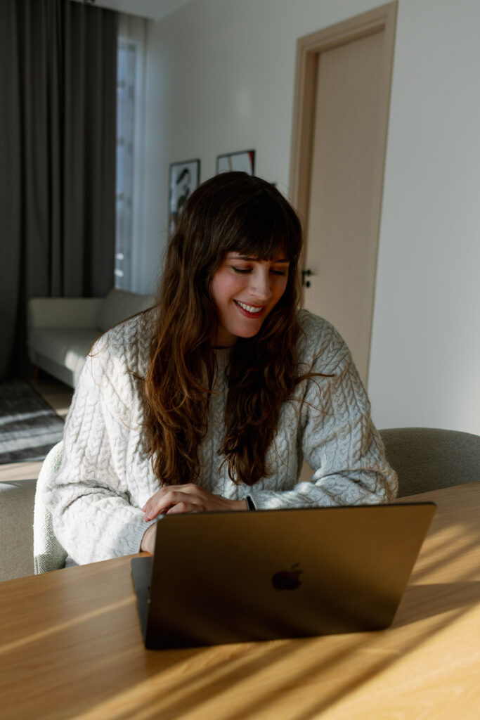 Andrea Funk arbeitet lächelnd am Laptop im Homeoffice und schreibt einen Blogartikel über Longevity und gesund alt werden
