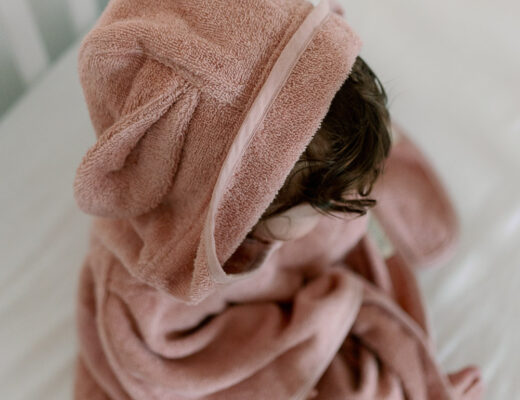 Baby im rosafarbenen Badeponcho auf dem Bett, Baby-Erstausstattung