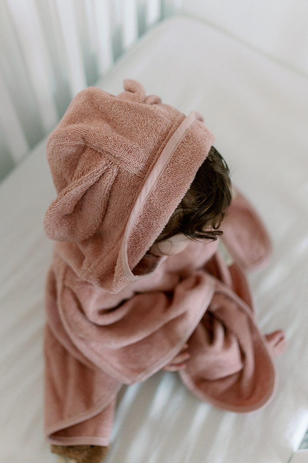 Baby im rosafarbenen Badeponcho auf dem Bett, Baby-Erstausstattung