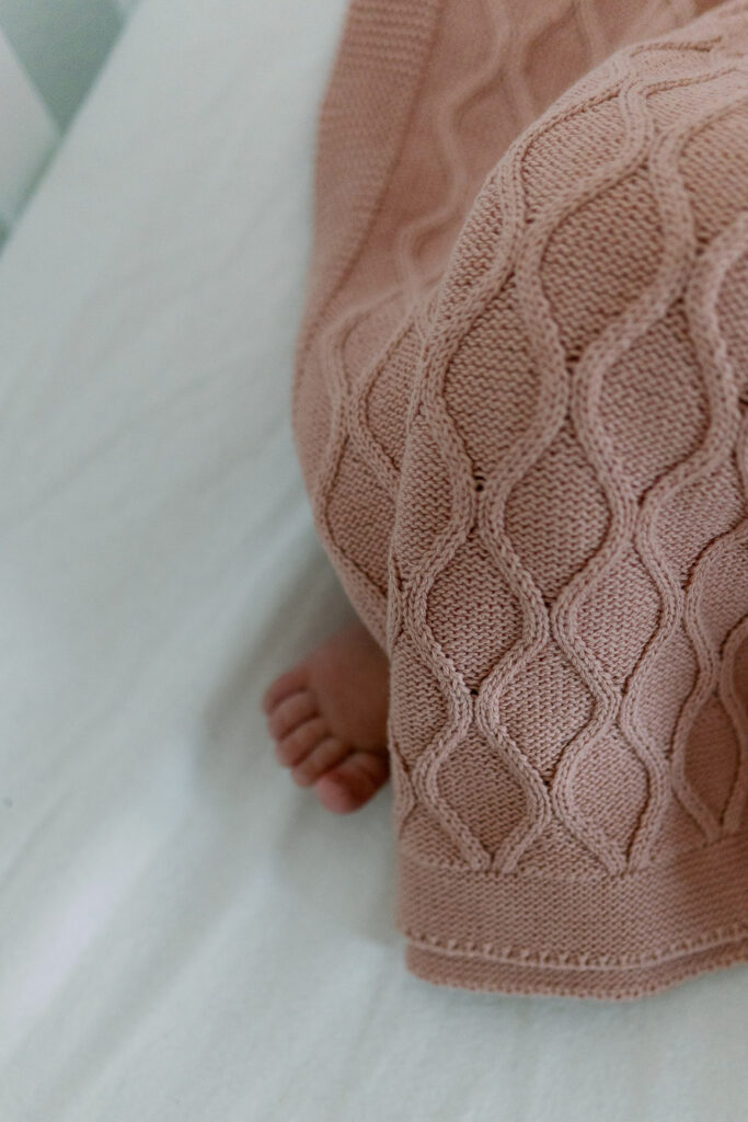 Babyfuß unter rosafarbener Strickdecke, Detailaufnahme im Babybett