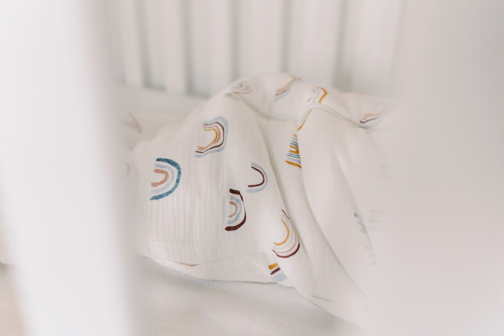 Schlafsack mit Regenbogenmuster liegt auf dem Bett, kuschelige Babyszene
