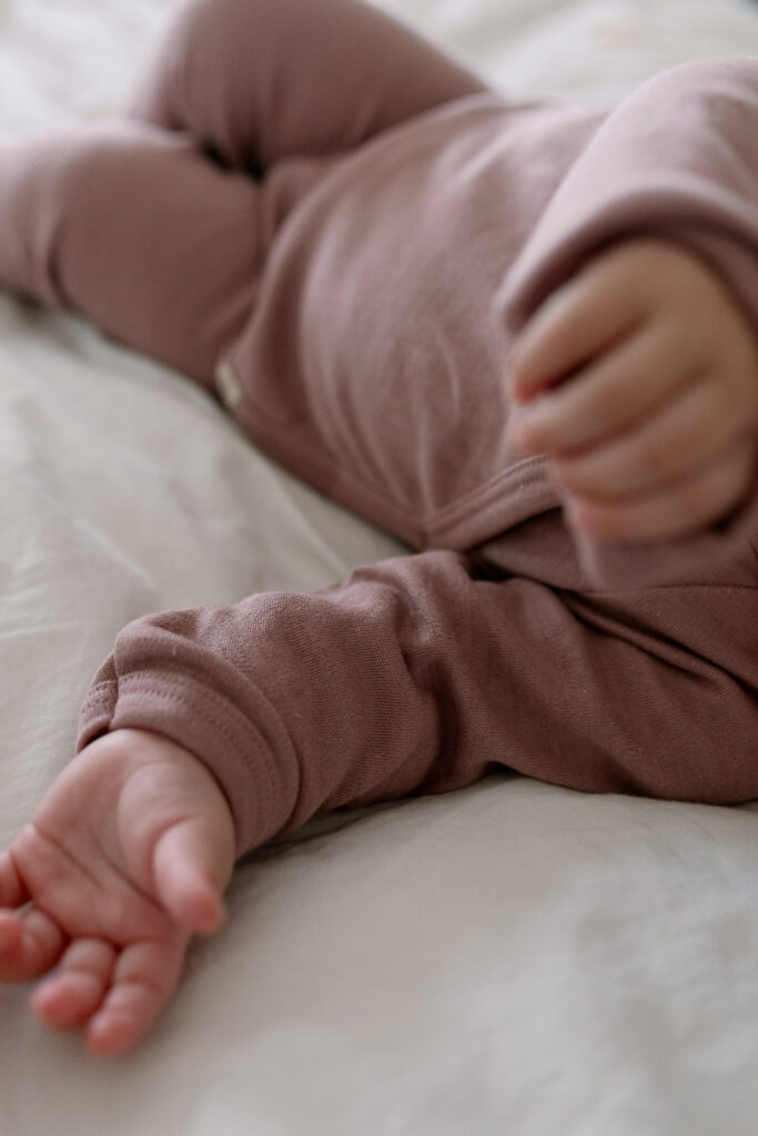 Detailaufnahme: Baby liegt auf heller Bettwäsche, kleine Hand und Fuß im Fokus