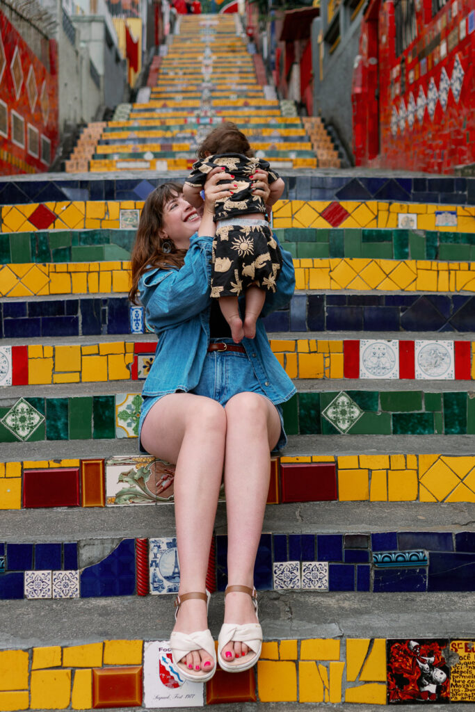 Geschenkideen für Kinder: Mama hebt ihr Baby auf einer bunten Treppe in Rio de Janeiro hoch