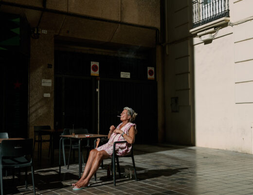 Reisefotografie für Anfänger: ältere Frau sitzt rauchend im Sonnenlicht eines Straßencafés in Valencia
