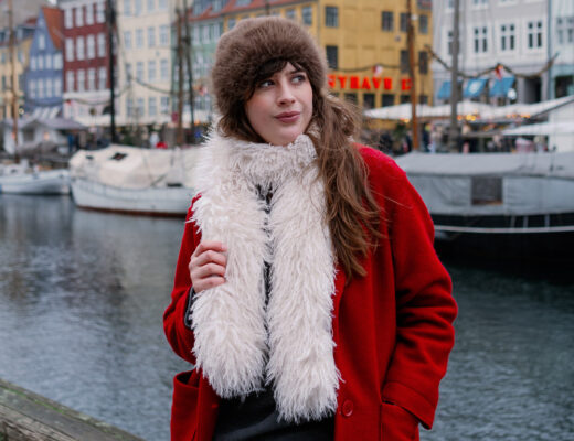 Andrea von andysparkles in rotem Mantel, Fake-Fur-Hut und flauschigem Schal am Hafen in Kopenhagen, Virale Winter Fashion Hacks für warmes Sightseeing