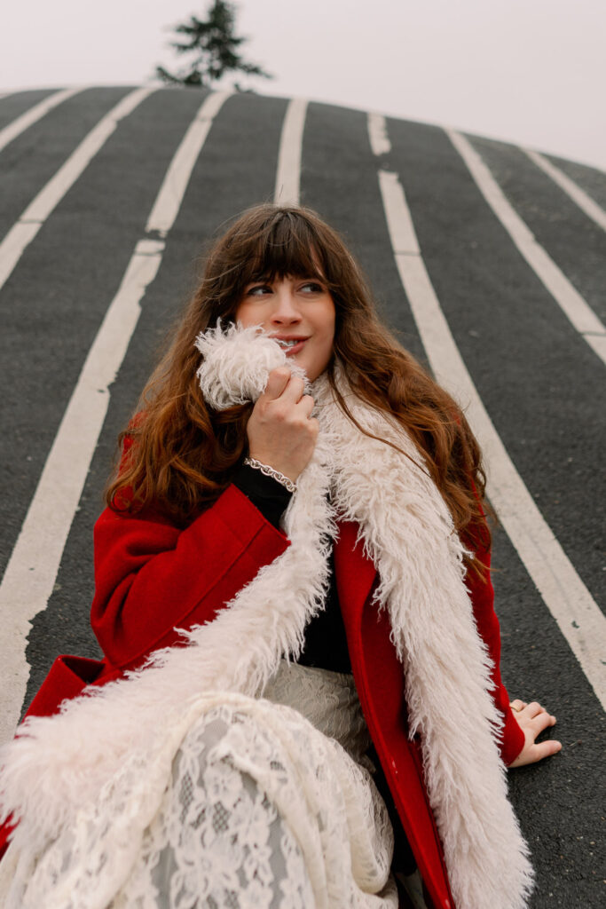 Andrea von andysparkles sitzt im Park Superkilen im roten Mantel und weißem Schal, Winterlook mit Spitzenrock bei kaltem Wetter