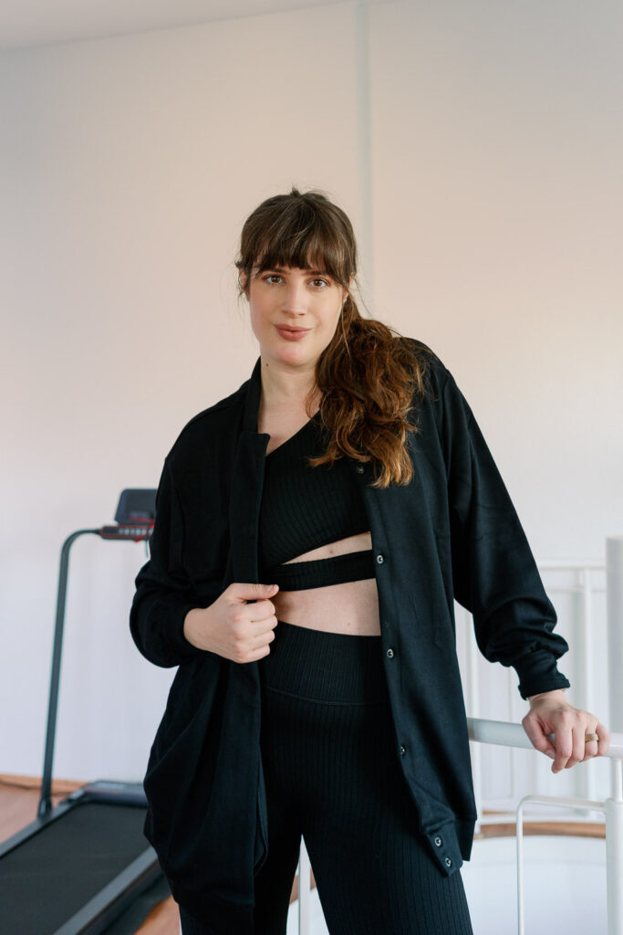 Elodie Athleisure Look mit Leggings und Top in Schwarz, Portrait indoor vor dem Laufband