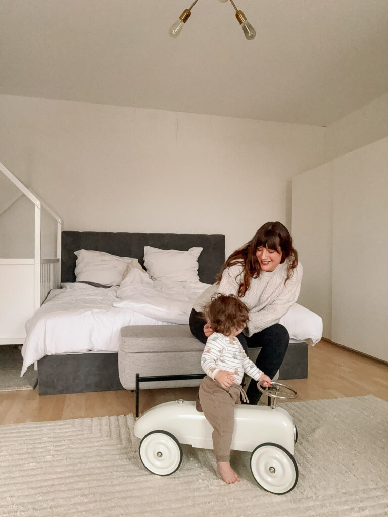 Andrea from andysparkles in the bright bedroom with her baby on a ride-on car - routine to combat lack of sleep as a mother.