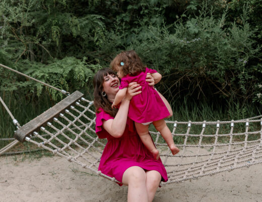 Andrea sitzt mit Dottie auf einer Hängematte im Park und sammelt Ideen für einen entspannten Kindergeburtstag draußen.