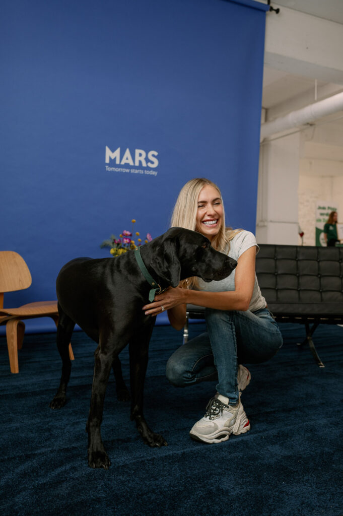 Alena Gerber hockt vor der Mars-Wand und umarmt eine schwarze Dogge beim Pressday zur Tieradoption
